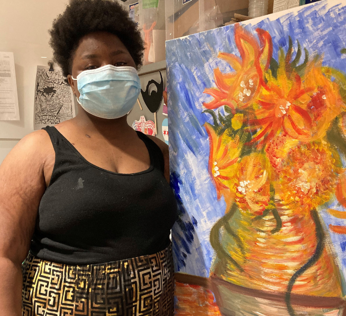 Young woman standing next to a colorful painting of flowers in a vase.