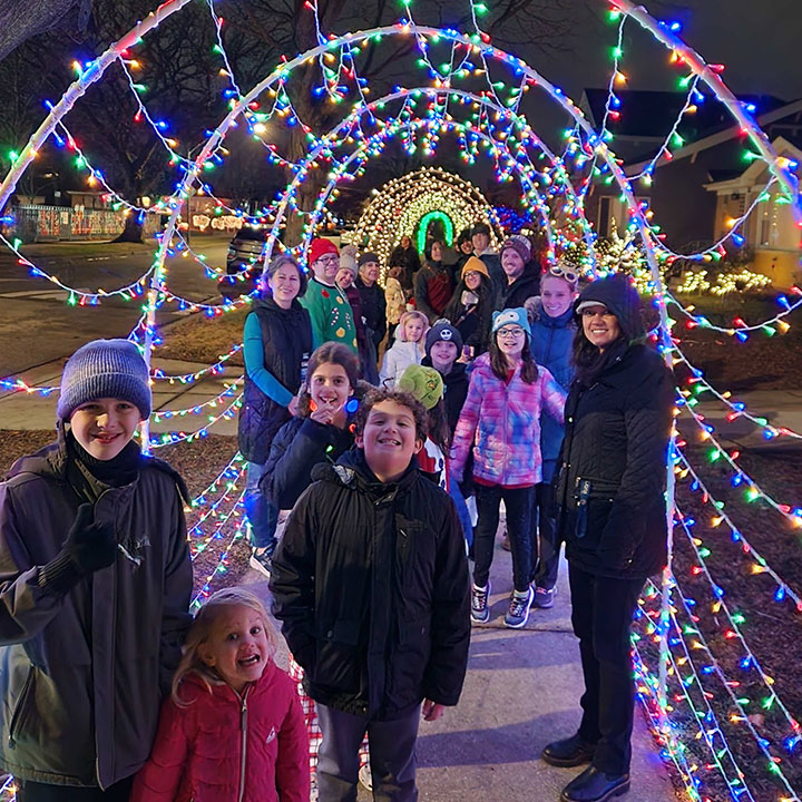 Group of community members gathered together outside under colorful decorative lights at a community gathering